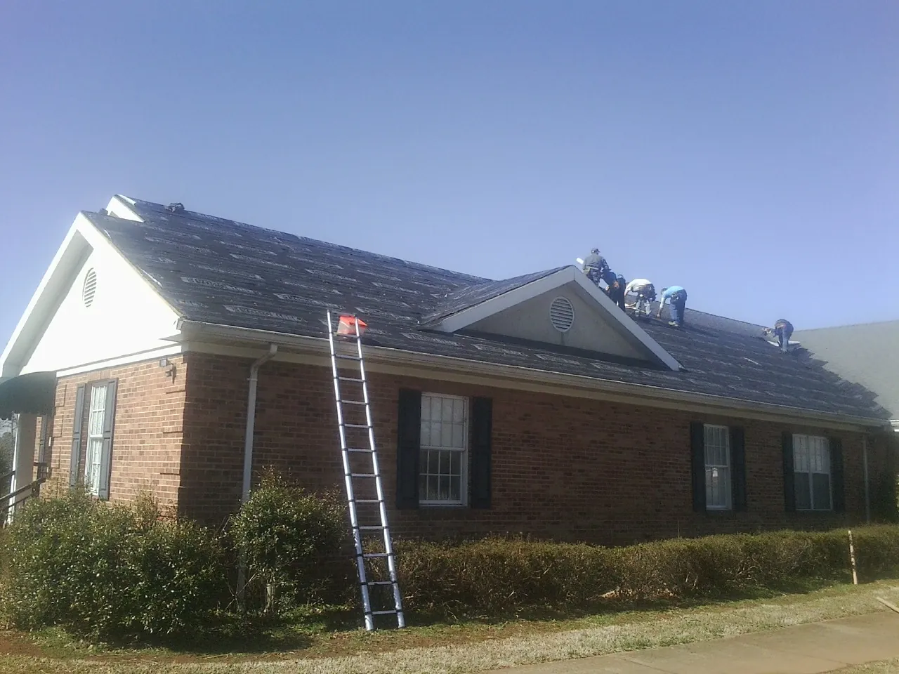 Crew tearing shingles off a brick ranch roof with a ladder set — Metal Roof Repair work by our crew in Peach Bottom