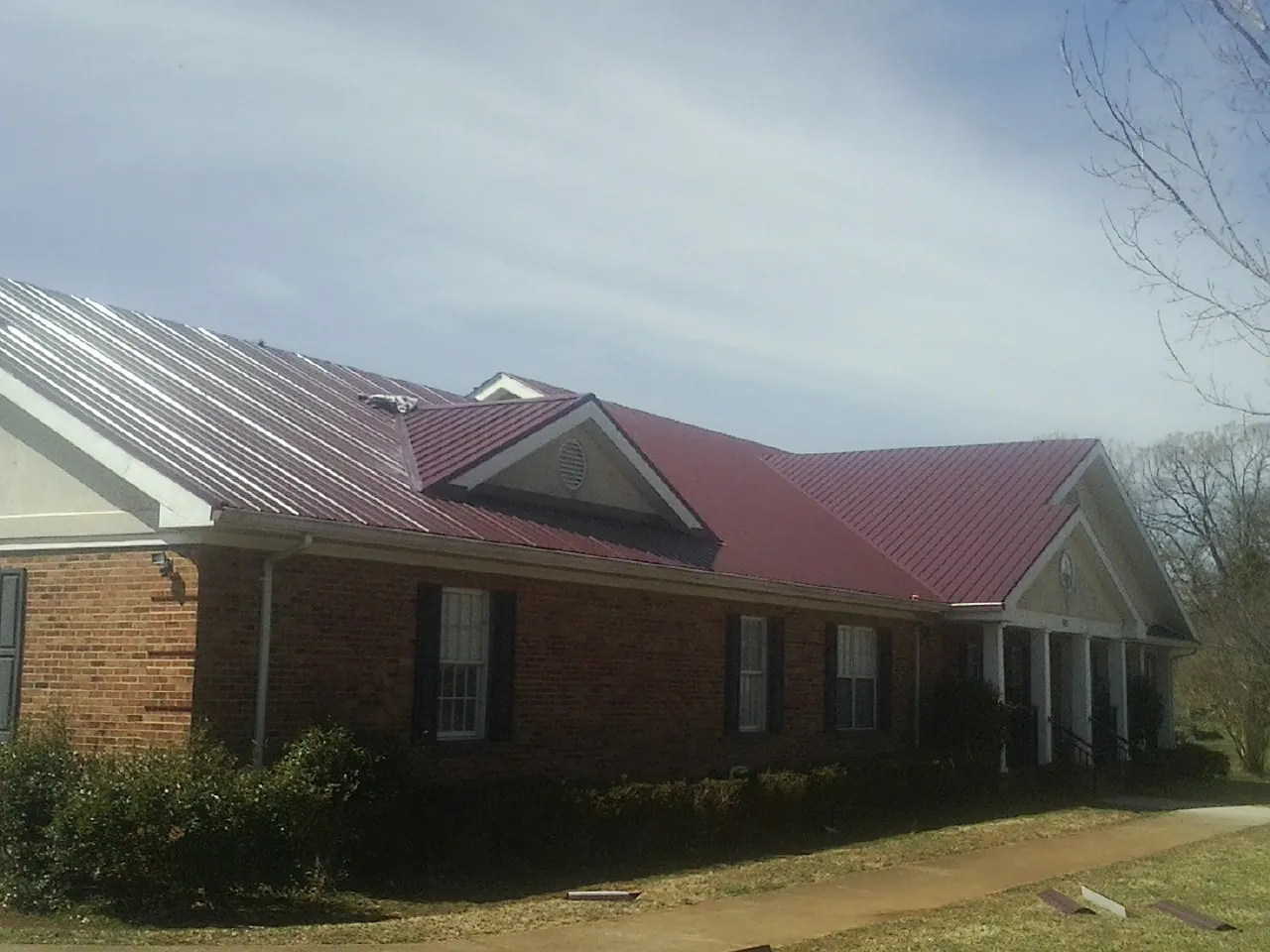 Red metal roof with gabled entries on a long brick building, from a Hail Damage Roof Repair job in Peach Bottom