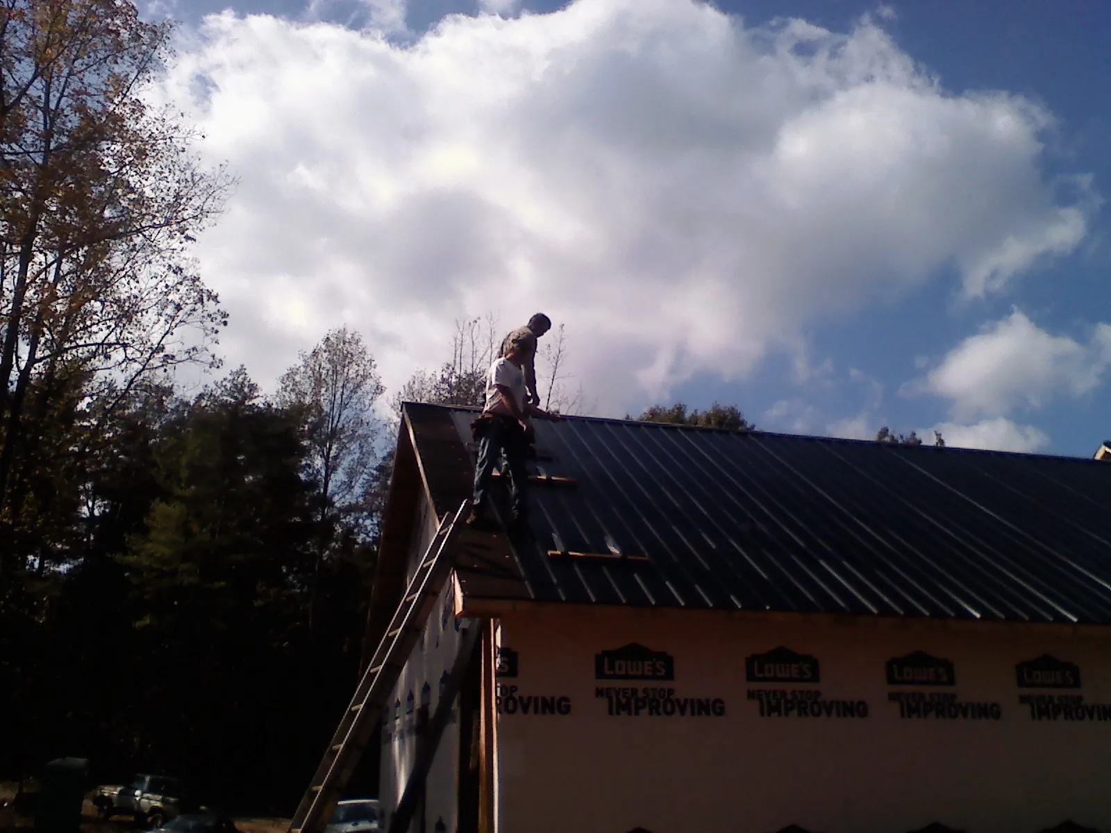 Roofer fastening dark metal panels high against a cloudy sky, from a Roof Inspection job in Peach Bottom