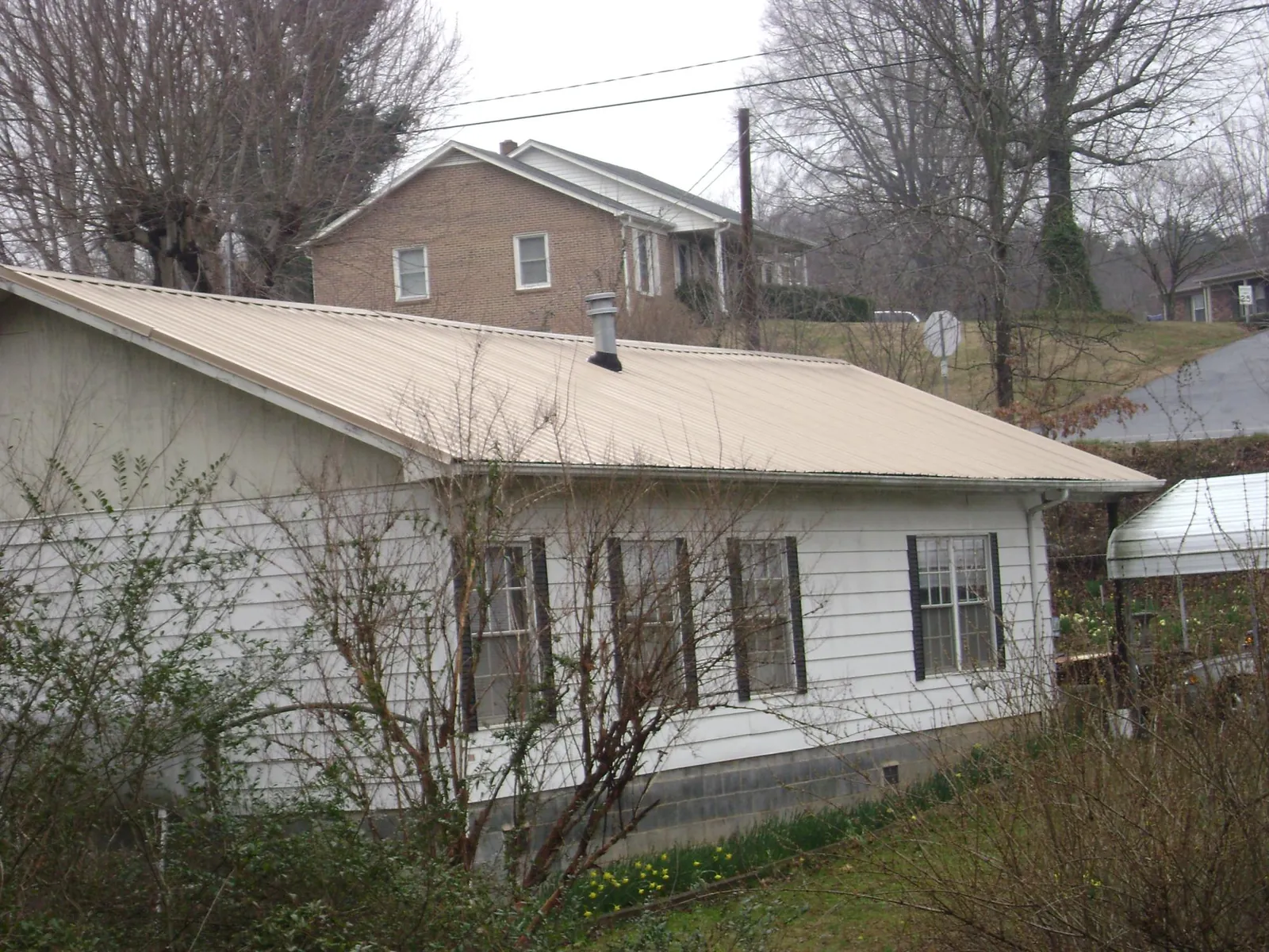 Tan metal roof on a white sided house set into a hillside — Commercial Roofing by Roofing Brothers in Peach Bottom